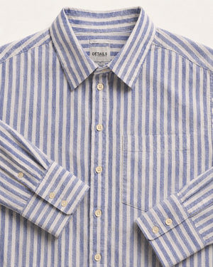 A close-up of a blue and white striped long-sleeve button-down shirt with a pointed collar, chest pocket, and light-colored buttons. The brand name 'DETAILS' is visible on the inner neck label.