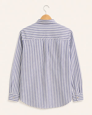 A long-sleeve striped button-up shirt hanging on a wooden hanger against a light cream background. The shirt features vertical stripes in blue and white, with a matching blue horizontal stripe panel across the upper back.