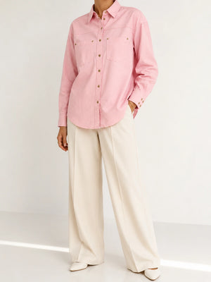 A model wearing a light pink long-sleeve button-up shirt with chest pockets and cream wide-leg trousers, standing against a clean white studio background.