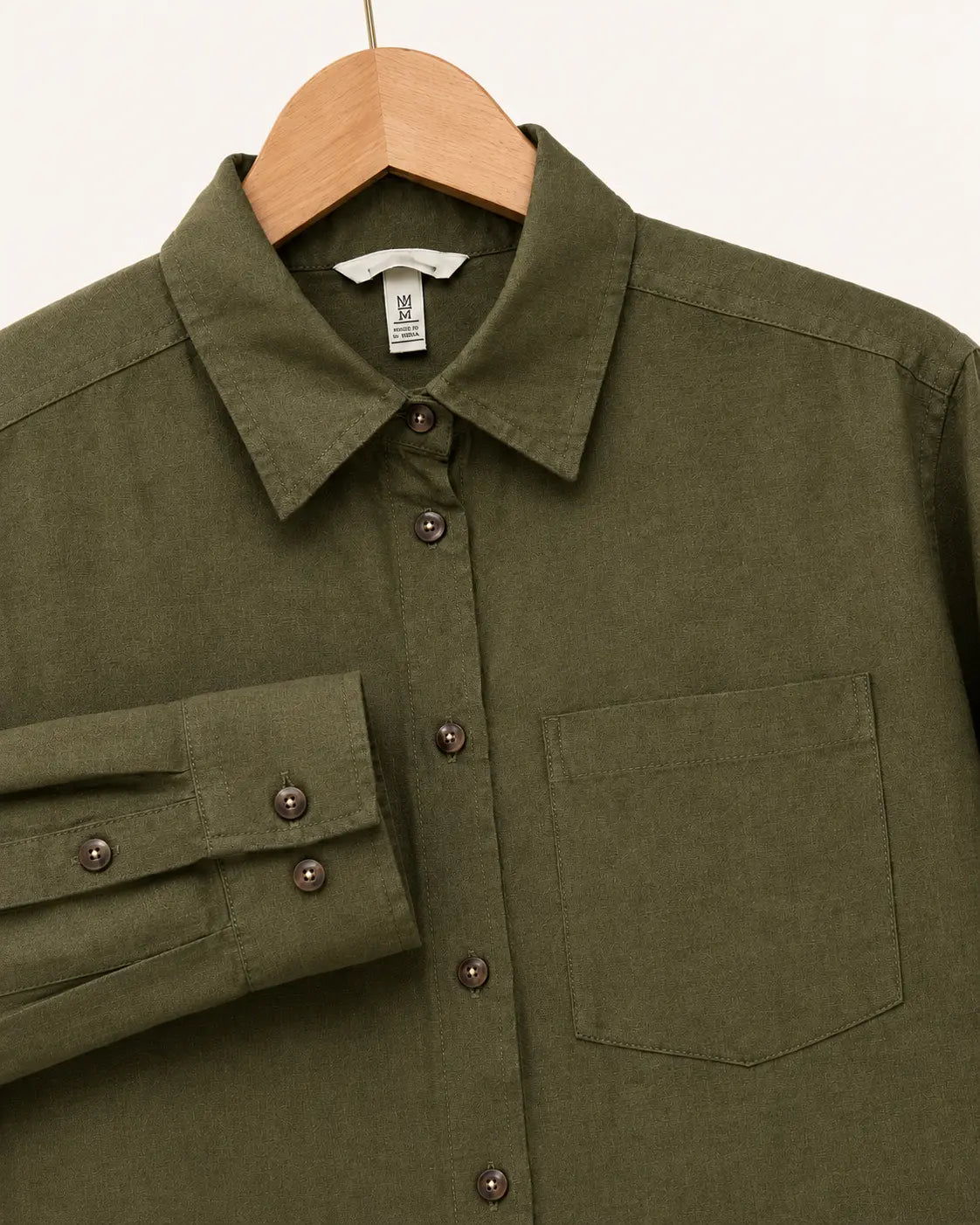 An olive green long-sleeve button-up shirt with a chest pocket and a folded cuff, hanging on a wooden hanger against a plain off-white background.