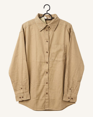 A beige long-sleeve button-up shirt with a pointed collar and a single chest pocket, hanging on a black hanger against a light cream background.