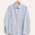 A long-sleeve button-up shirt with vertical blue and white stripes, hanging on a wooden hanger against a light beige background.