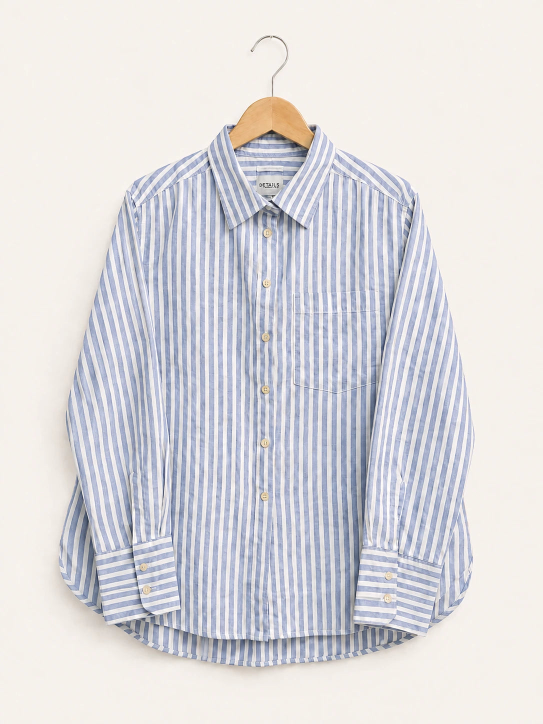 A long-sleeve button-up shirt with vertical blue and white stripes, hanging on a wooden hanger against a light beige background.