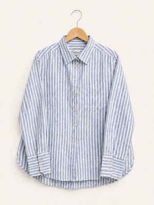 A long-sleeve button-up shirt with vertical blue and white stripes, hanging on a wooden hanger against a light beige background.