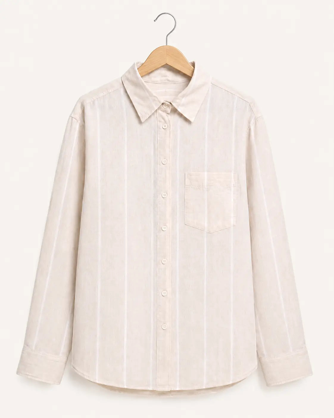 A light beige long-sleeve button-up shirt with thin white vertical stripes, featuring a pointed collar and a single chest pocket, hanging on a wooden hanger against a solid off-white background.
