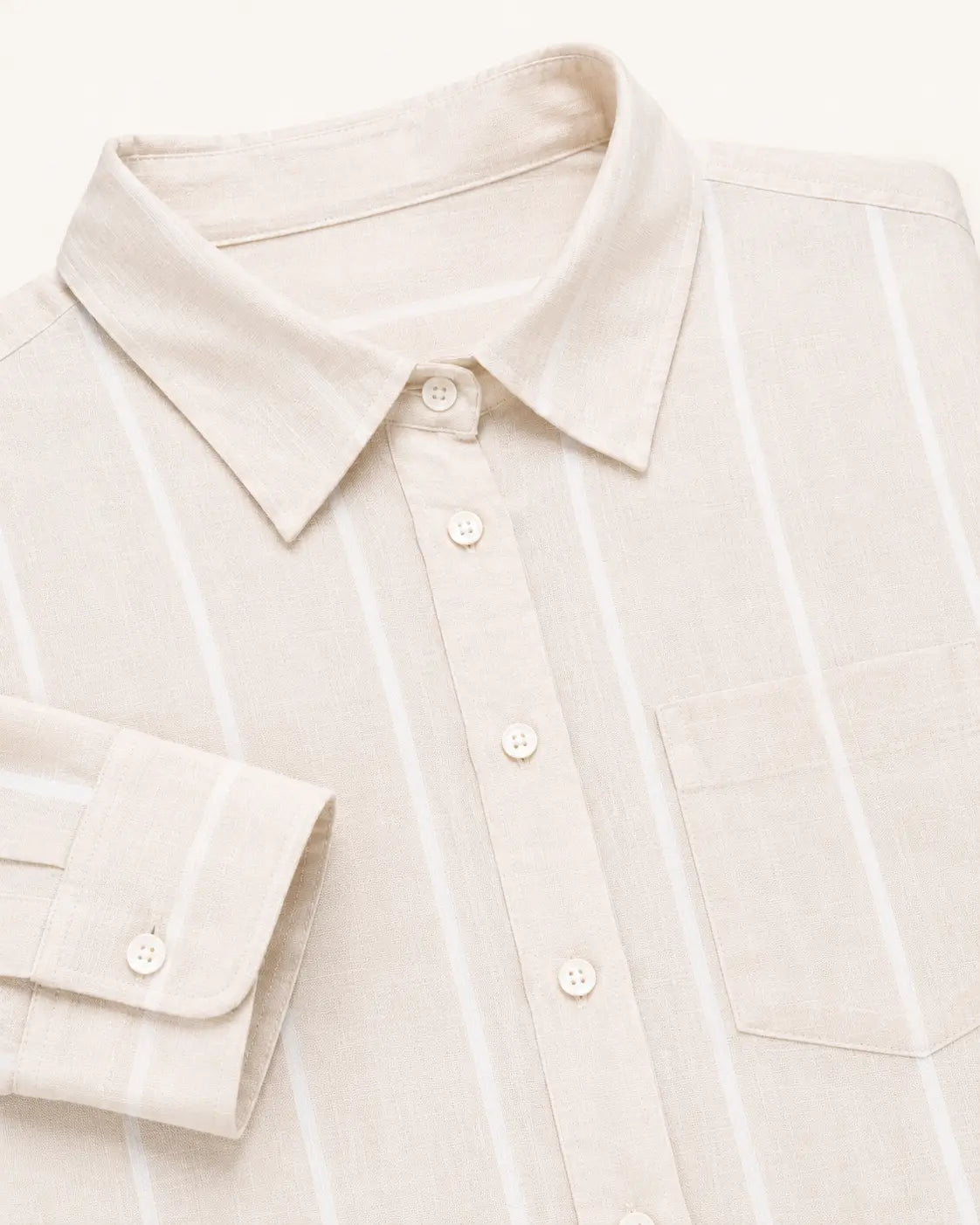 Close-up of a light beige linen button-down shirt with thin white vertical stripes, featuring a pointed collar, a chest pocket, and a folded cuff with a button.