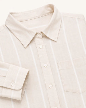 Close-up of a light beige linen button-down shirt with thin white vertical stripes, featuring a pointed collar, a chest pocket, and a folded cuff with a button.