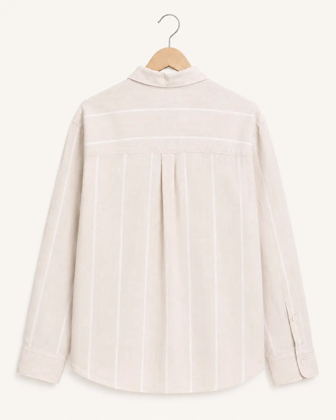 A light beige linen shirt with vertical white stripes, hanging on a wooden hanger against a solid cream background.