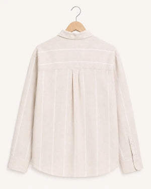 A light beige linen shirt with vertical white stripes, hanging on a wooden hanger against a solid cream background.