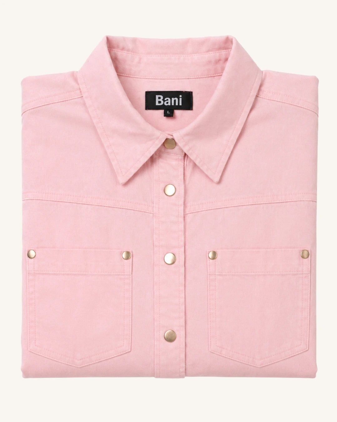 A folded light pink long-sleeve button-up shirt with two chest pockets and gold-tone metal snap buttons, shown on a plain off-white background. The brand label 'Bani' is visible inside the collar.