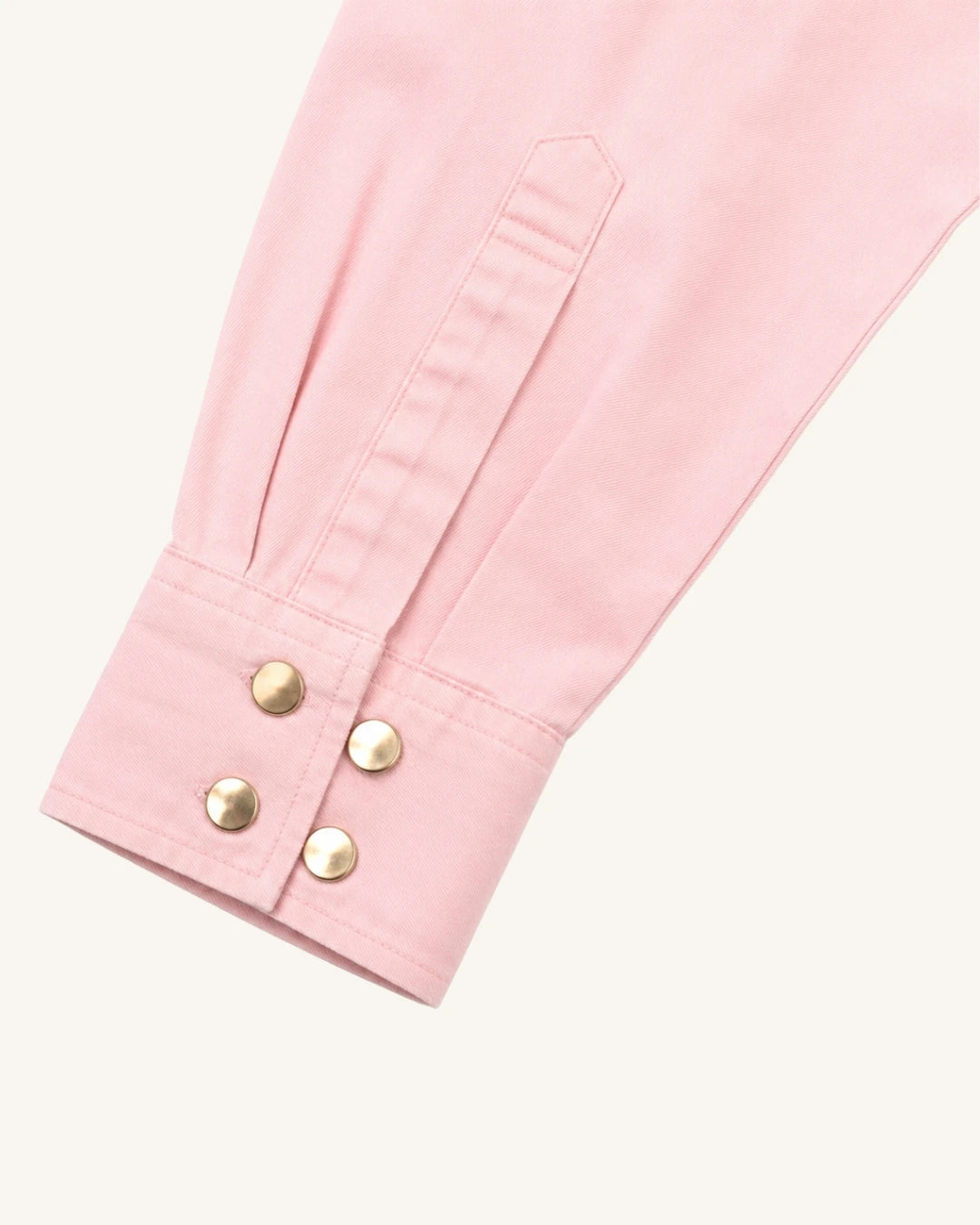 A close-up of a light pink garment sleeve with a buttoned cuff and four gold-tone snap buttons, shown on a plain off-white background.