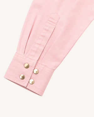 A close-up of a light pink garment sleeve with a buttoned cuff and four gold-tone snap buttons, shown on a plain off-white background.