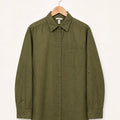 An olive green long-sleeve button-up shirt with a chest pocket and button details on the cuffs, hanging on a wooden hanger against a plain off-white background.