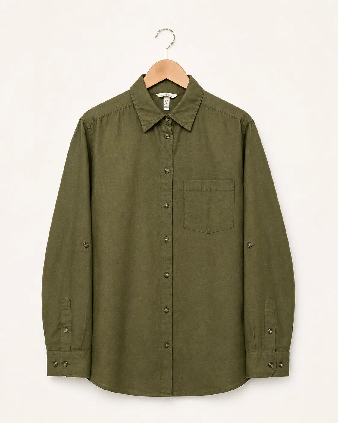 An olive green long-sleeve button-up shirt with a chest pocket and button details on the cuffs, hanging on a wooden hanger against a plain off-white background.