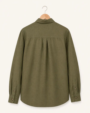 An olive green long-sleeve button-up shirt shown from the back, hanging on a wooden hanger against a light beige background.