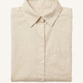 A folded light beige linen button-up shirt with a classic collar and a single chest pocket, displayed on a clean off-white background.