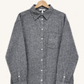 A dark gray textured long-sleeve button-up shirt with a chest pocket, hanging on a wooden hanger against a light cream background.