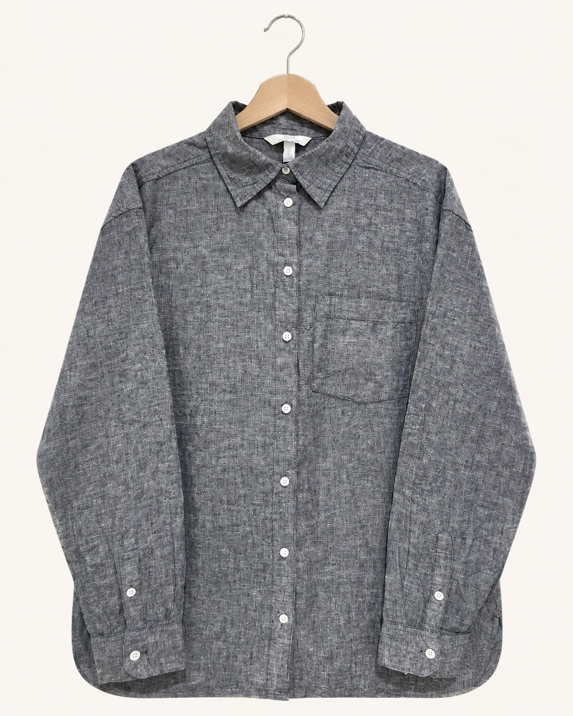 A dark gray textured long-sleeve button-up shirt with a chest pocket, hanging on a wooden hanger against a light cream background.
