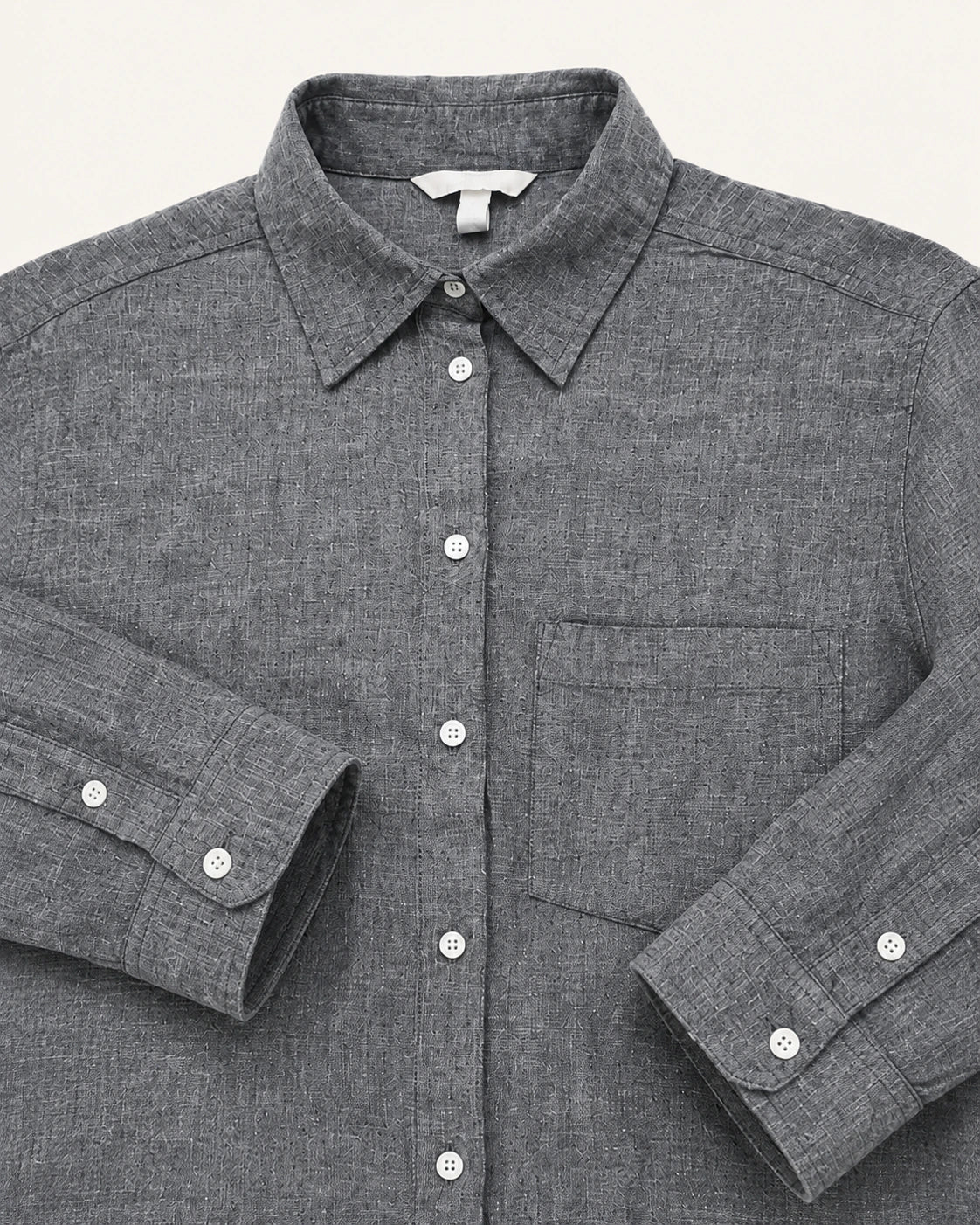 A close-up of a dark gray textured linen shirt with a pointed collar, button-down front, and a chest pocket, laid flat against a light off-white background.