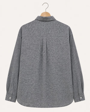 A gray textured long-sleeve button-up shirt shown from the back, hanging on a wooden hanger against a light cream background.