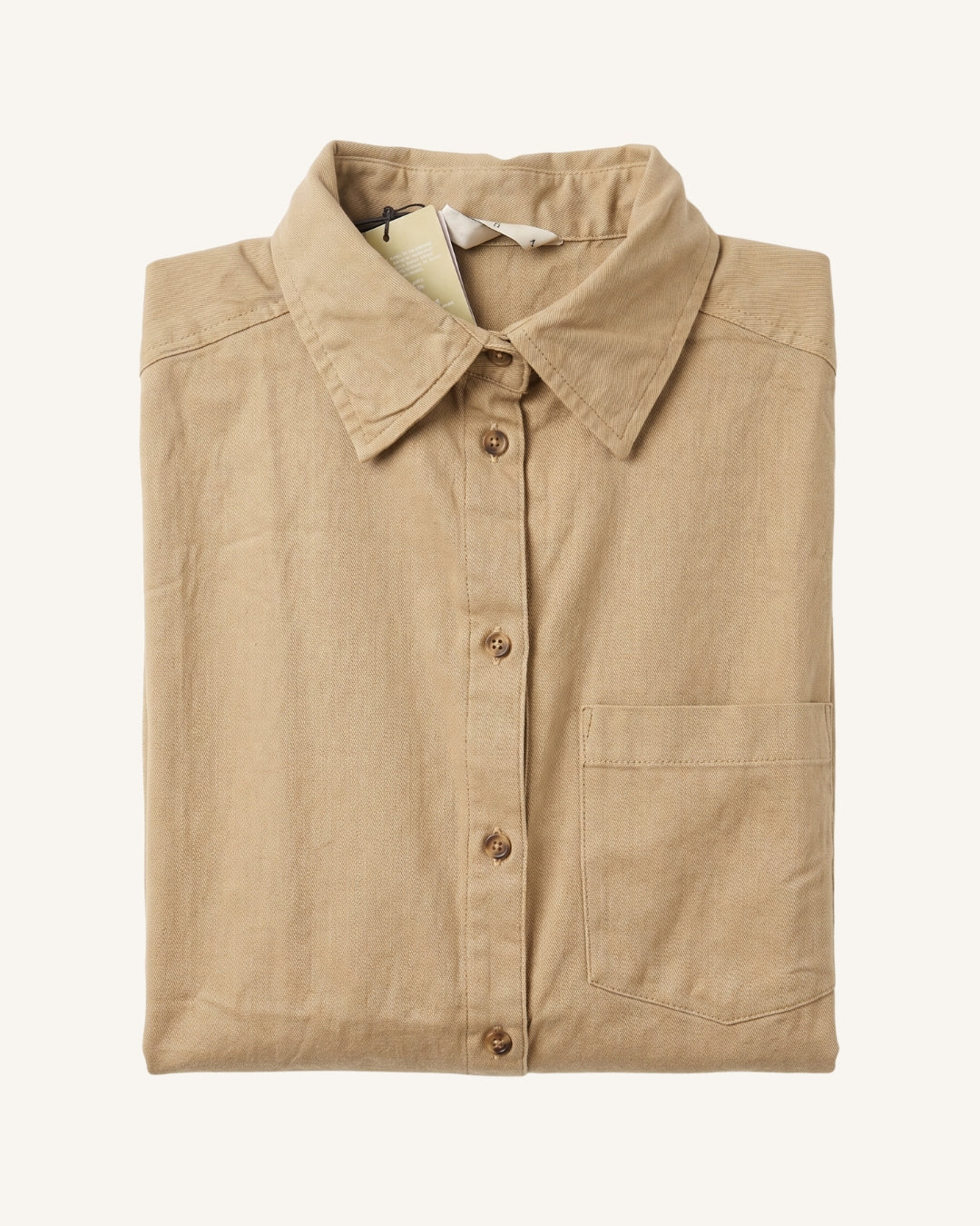 A folded tan linen button-up shirt with a classic collar and a single chest pocket, displayed on a clean off-white background.
