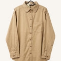 A beige long-sleeve button-up shirt with a pointed collar and a single chest pocket, hanging on a black hanger against a light cream background.